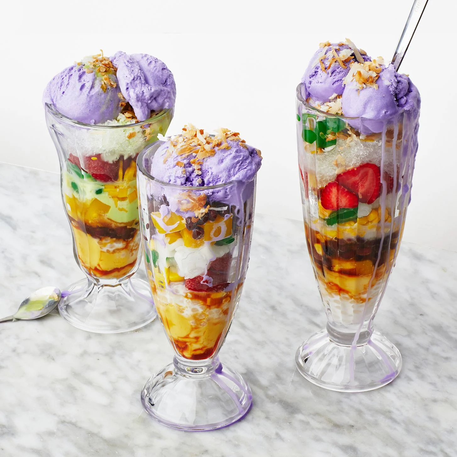 Three glasses of Filipino halohalo layered with mango jelly fruit flan shaved ice and ube ice cream.