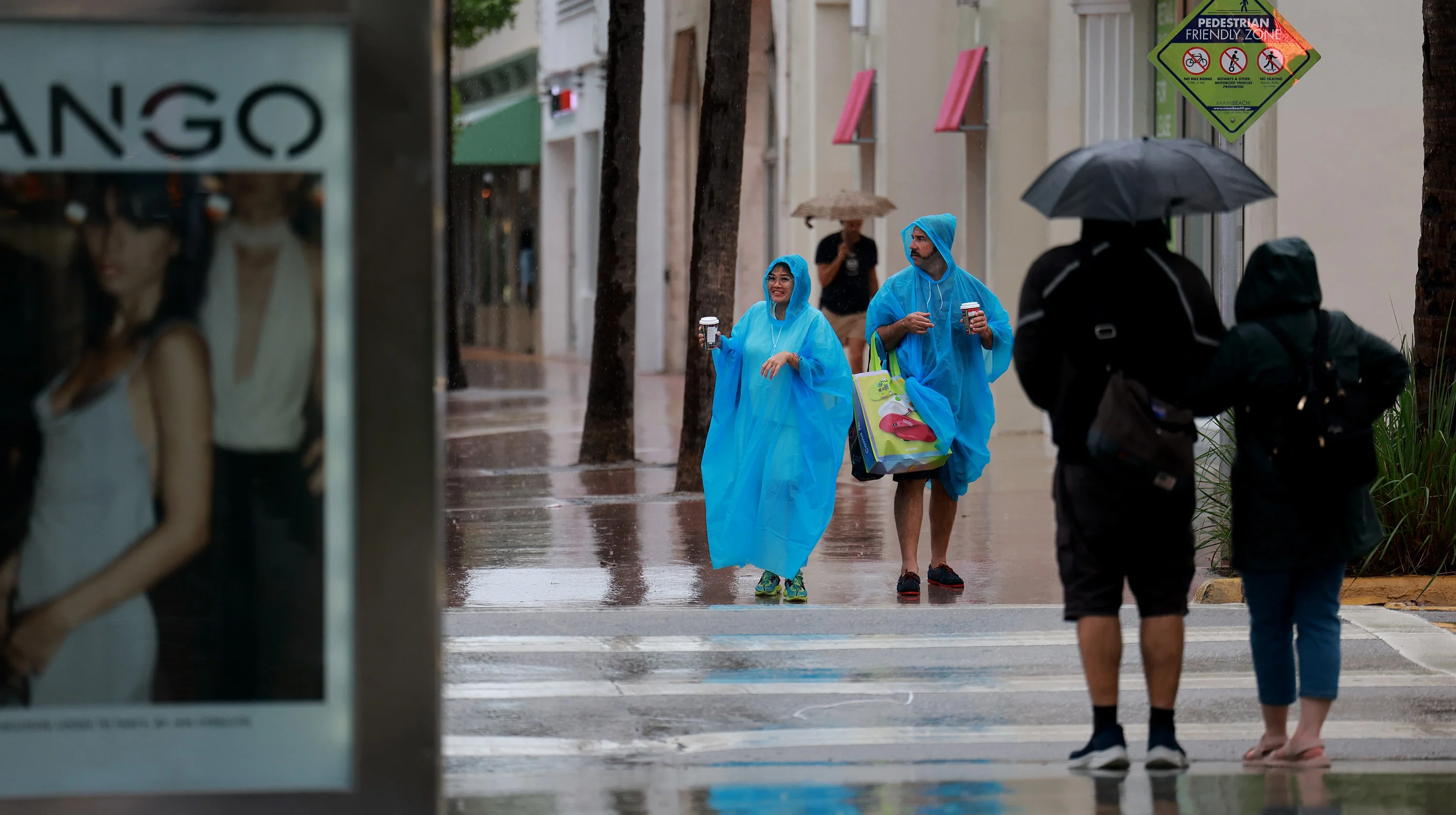 MIAMI BEACH, Florida — NOVEMBER 15: Pedestrians try to stay dry as rain inundates the area on Nov. 15, 2023 in Miami Beach, Florida. A weather system slowly passing through South Florida is leaving Miami-Dade soaked and causing concern for potential flooding. (Photo by Joe Raedle/Getty Images)