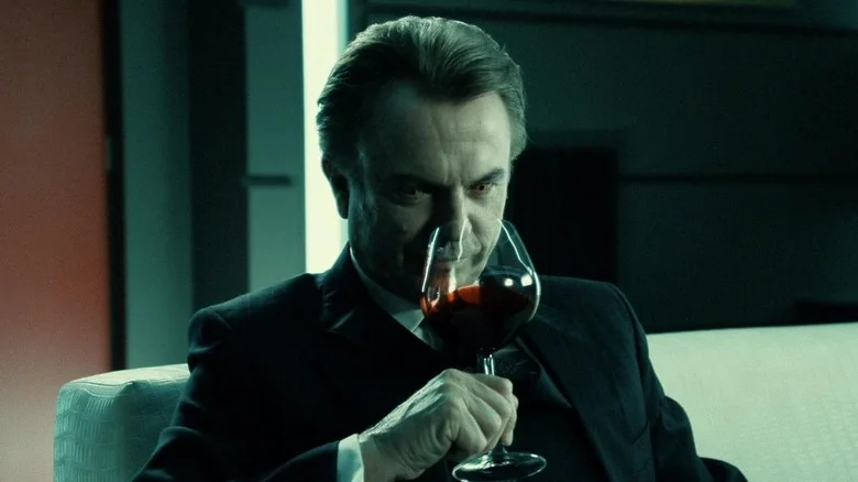 Sam Neill as Charles Bromley sipping a glass of red liquid in Daybreakers