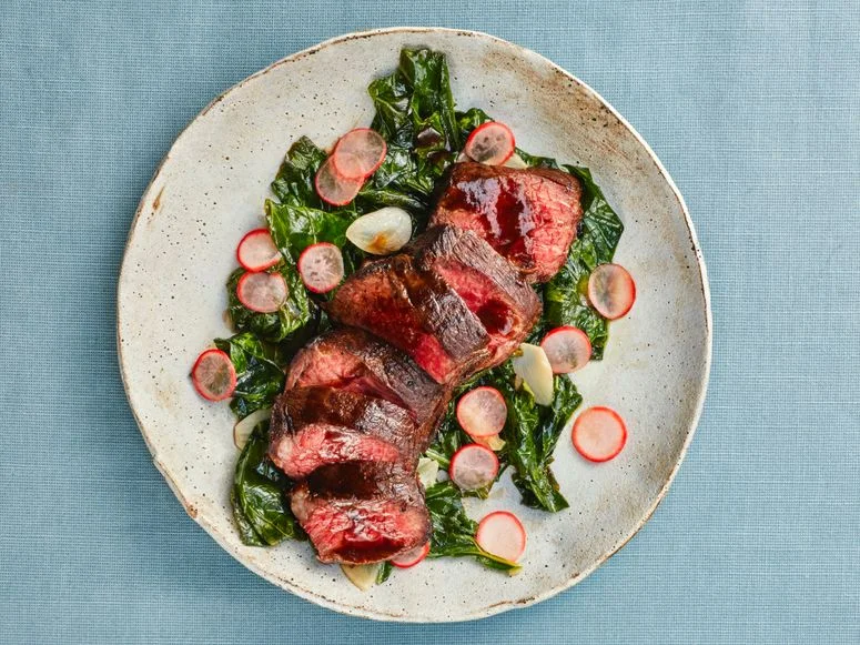 Chris's Steak for 1 plated on top of bright green colllards topped with sliced radishes.