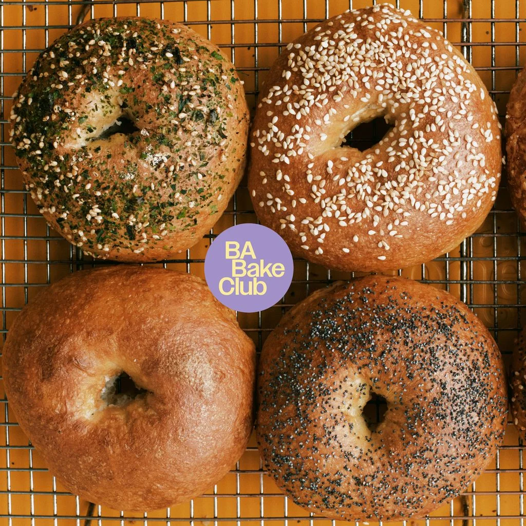 Six bagels on a wire rack topped with furikake sesame seeds melted Parmesan poppy seeds and everything bagel topping.