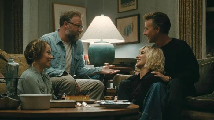 Four people sit laughing together in a cozy living room, suggesting a humorous or joyful moment from a TV or movie scene