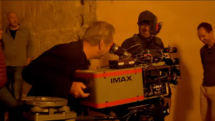 Person operating an IMAX camera on a film set, surrounded by crew members who are engaged and smiling