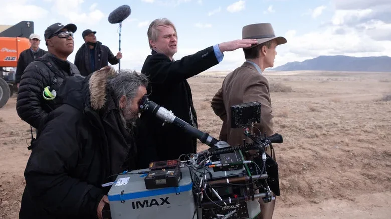 Christopher Nolan points into the distance as he stands with a camera crew behind the scenes of Oppenheimer