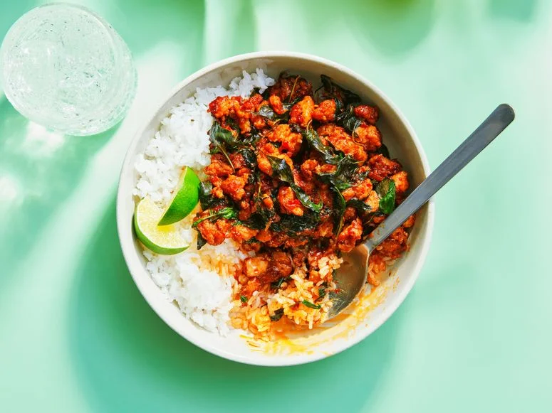 Basil and ground chicken on white rice in a white bowl