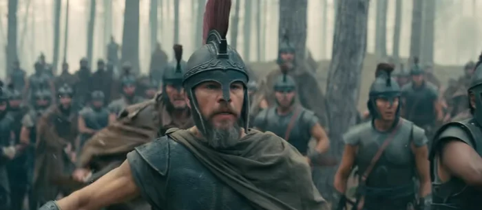Battle scene with a bearded warrior in armor and a helmet leading troops in a forest setting