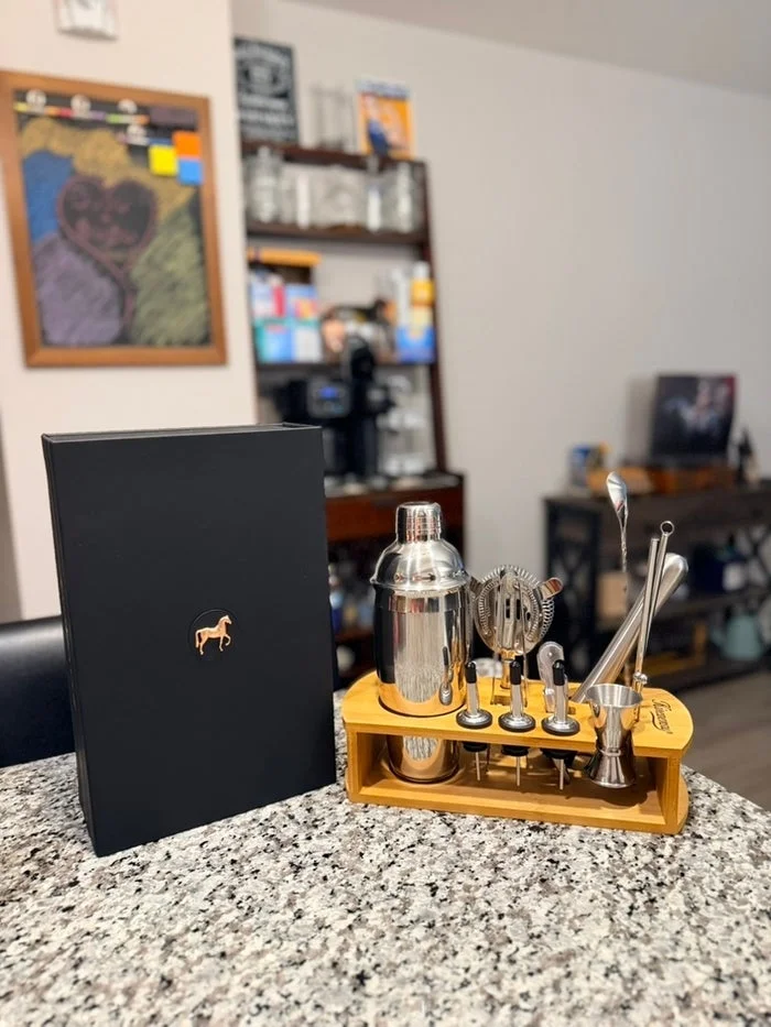Cocktail shaker set with various tools displayed on a kitchen counter, alongside a black box with a gold horse emblem