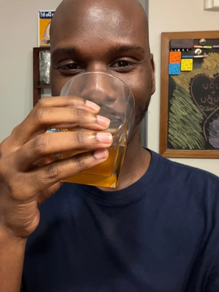 Person drinking from a glass, holding it close to their face, with a chalkboard visible in the background