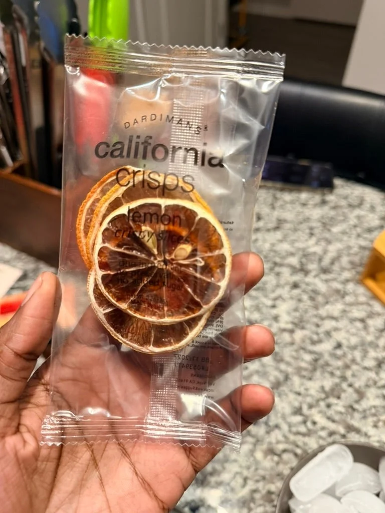 Packaged dried lemon slices labeled "California Crisps, Lemon" held by a person over a kitchen countertop