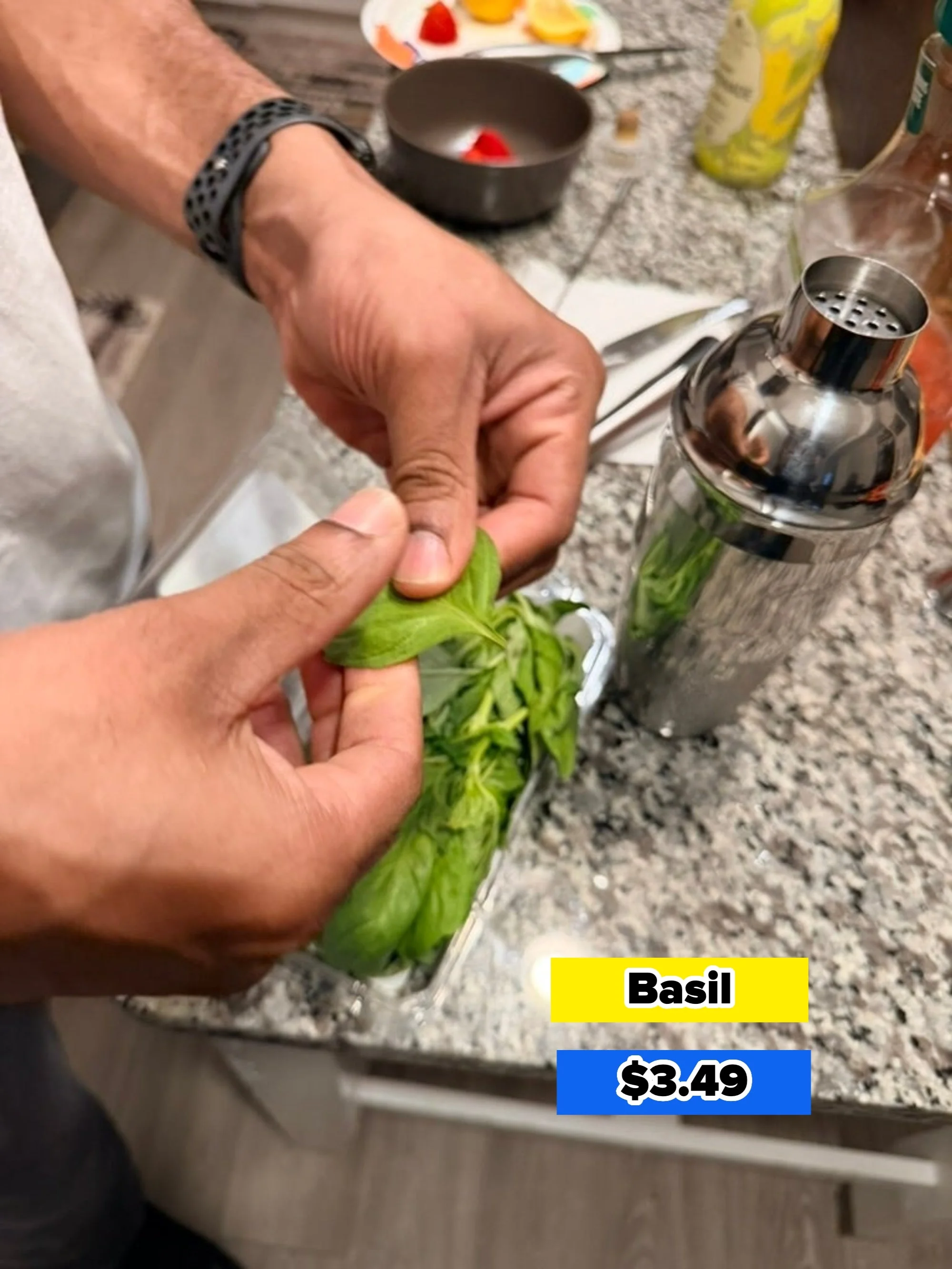 Person tearing fresh basil leaves in a kitchen, with a cocktail shaker and ingredients nearby