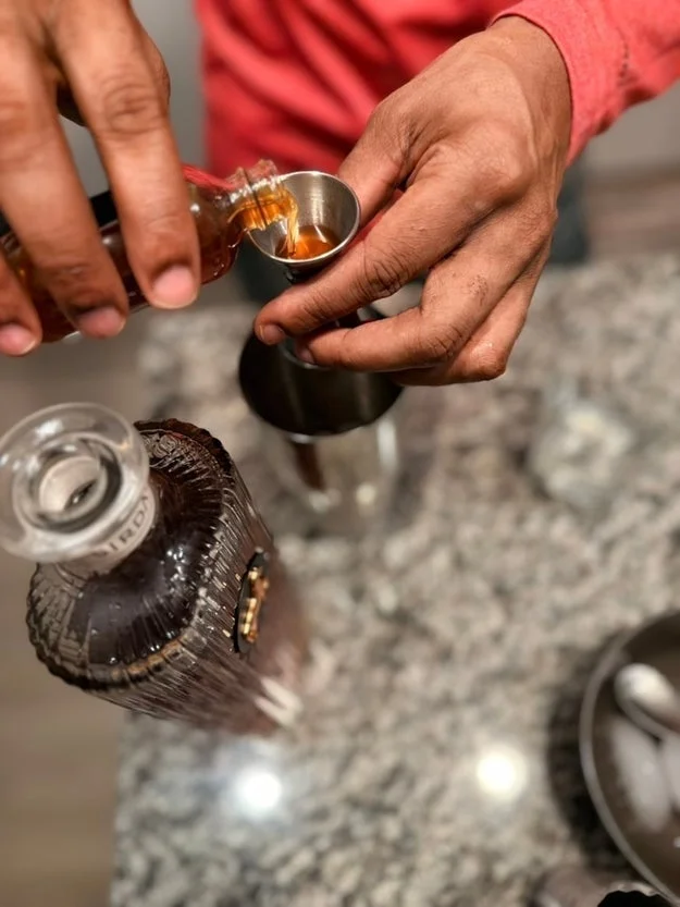 Person pouring liquor from a bottle into a jigger over a counter