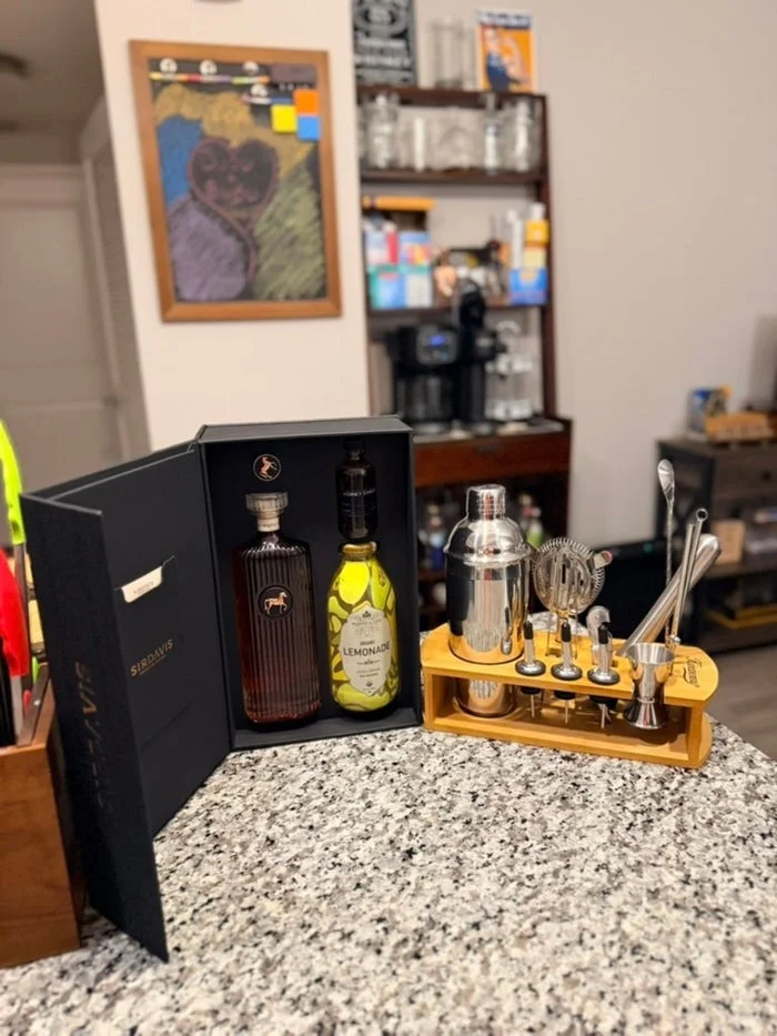Cocktail set with liquor bottle, limoncello, shaker, and bar tools on a countertop. Kitchen items visible in the background