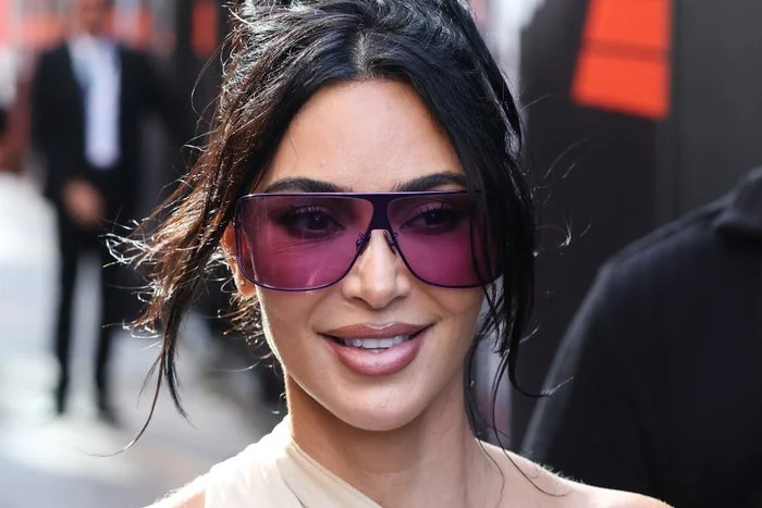 Kim Kardashian with long hair wearing large, stylish sunglasses and a chic outfit at a public event