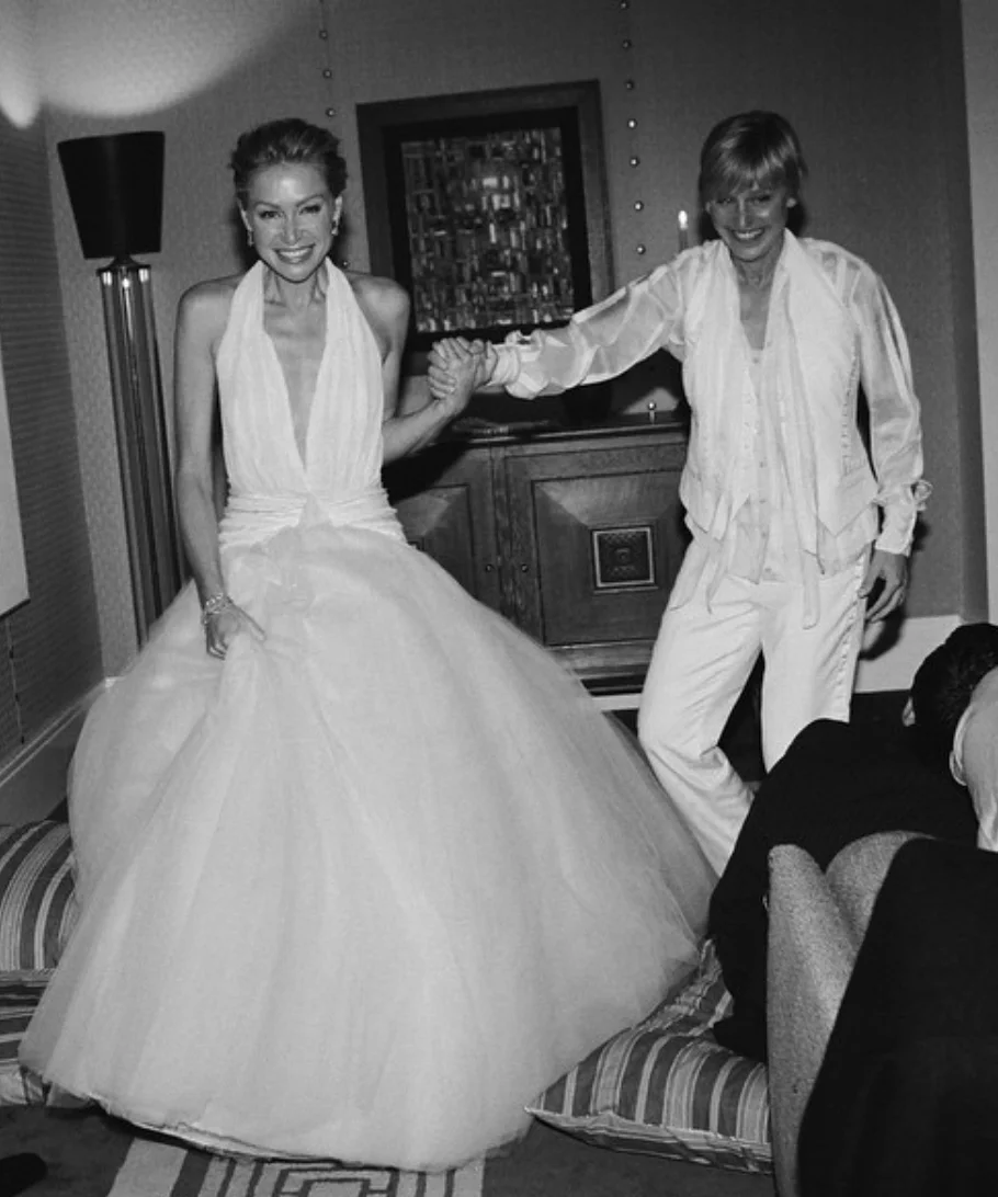 Two people in classic wedding attire, with one wearing a ball gown and the other in a suit. They are smiling and holding hands indoors