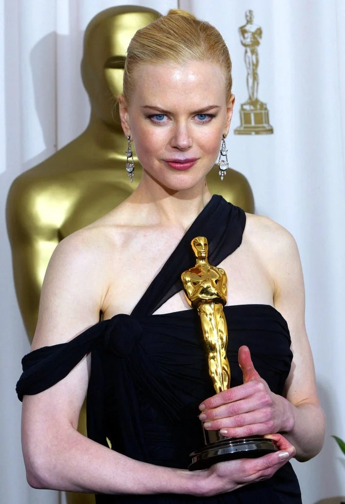 Nicole Kidman holds an Academy Award in a black evening gown with a slick updo