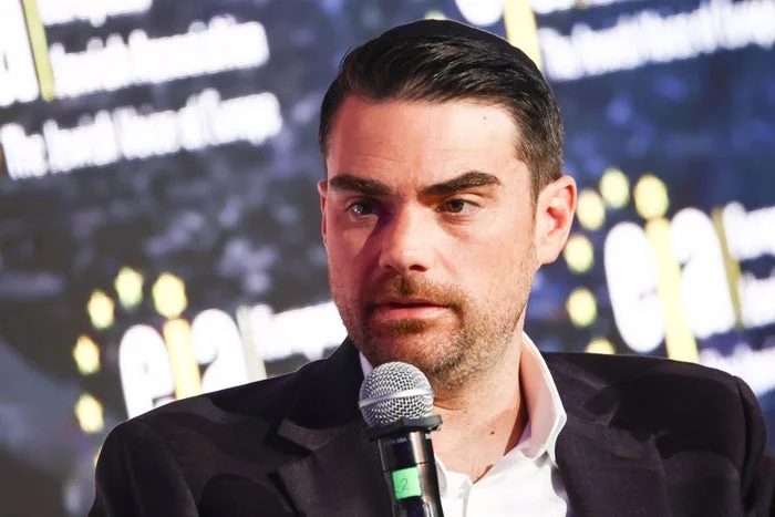 Person speaking into a microphone at a public event, wearing a suit jacket and shirt