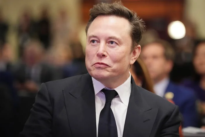A person in a suit and tie at an event, looking to the side with a thoughtful expression