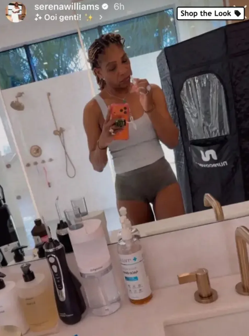 Serena in a bathroom taking a mirror selfie, wearing a tank top and shorts