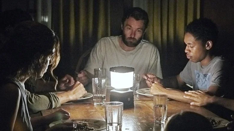 Paul, Sarah, and Kim around a table lit by a lantern in It Comes at Night