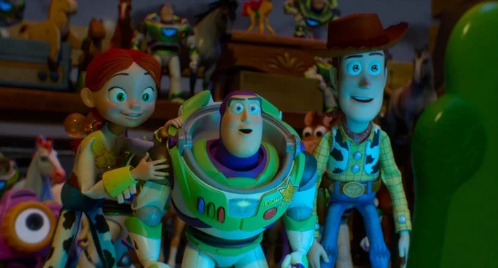 Animated characters Jessie, Buzz Lightyear, and Woody from Toy Story look excitedly at something off-screen. Various toys fill the background