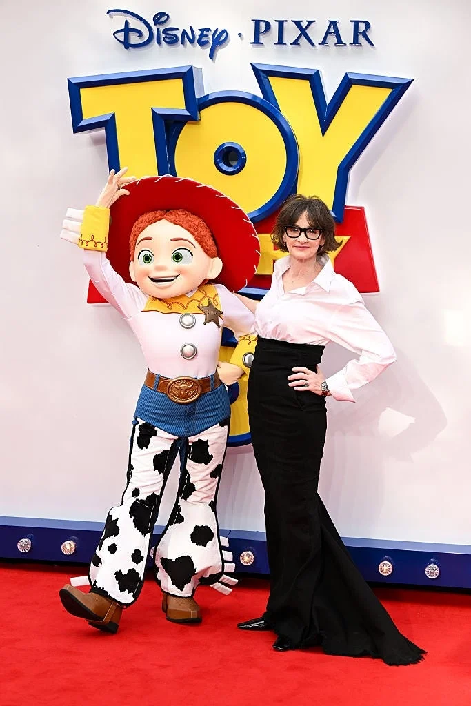 Person in elegant black skirt and white blouse poses with Toy Story character Jessie on a red carpet at a Disney Pixar event