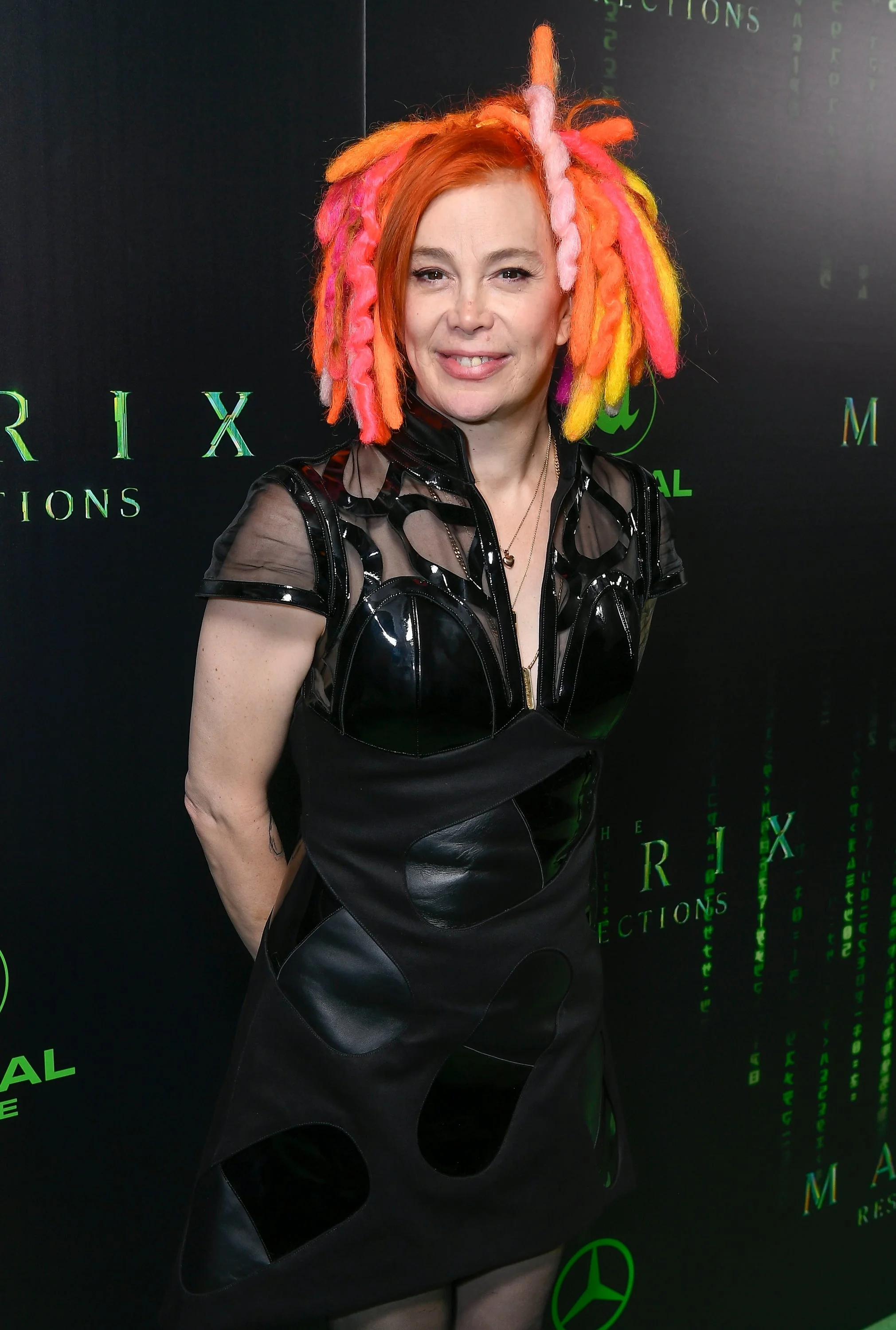 Person in a futuristic black dress with colorful, textured hair on a red carpet at a Matrix-themed event