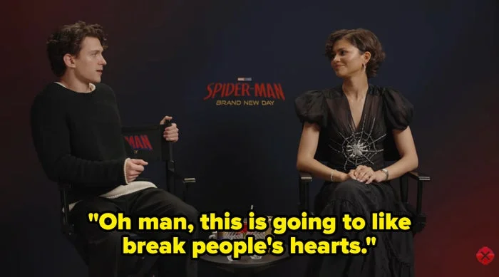 Tom and Zendaya sit in director's chairs at a media event for "Spider-Man: Brand New Day." One wears a casual outfit, the other a dress with a spiderweb design