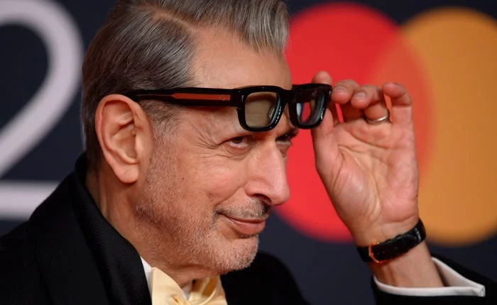 Close-up of Jeff Goldblum lifting his glasses while smirking