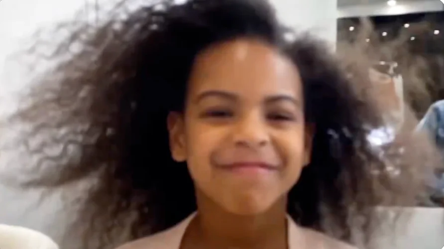 Child smiling with hair gently blowing, wearing a light-colored top