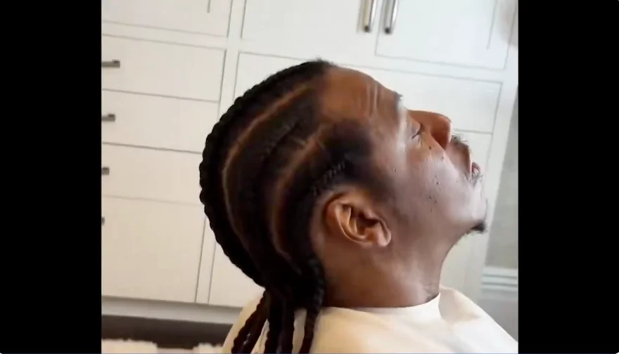 Person with braided hairstyle sits and looks upward, possibly in a salon. Their expression is calm and relaxed