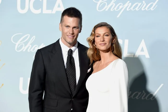 A man in a suit and tie stands with a woman in an elegant white dress at a formal event in front of a backdrop with logos
