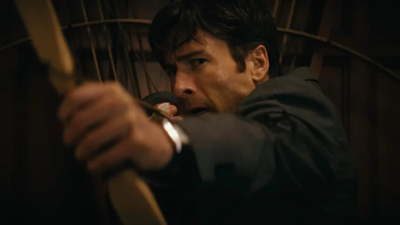 Glen Powell's Becket Redfellow aims a bow and arrow in closeup in How to Make a Killing