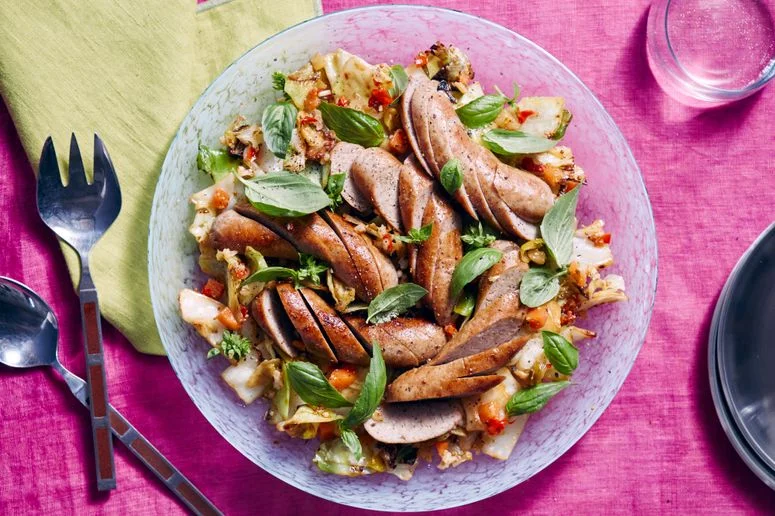 A plate of sliced sausage atop a bed of charred cabbage and giardiniera all on a clear decorative plate.