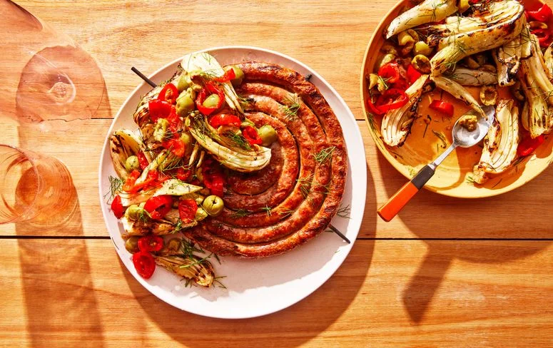 sausage dish on plate on wooden surface with side dish of fennel salad with spoons