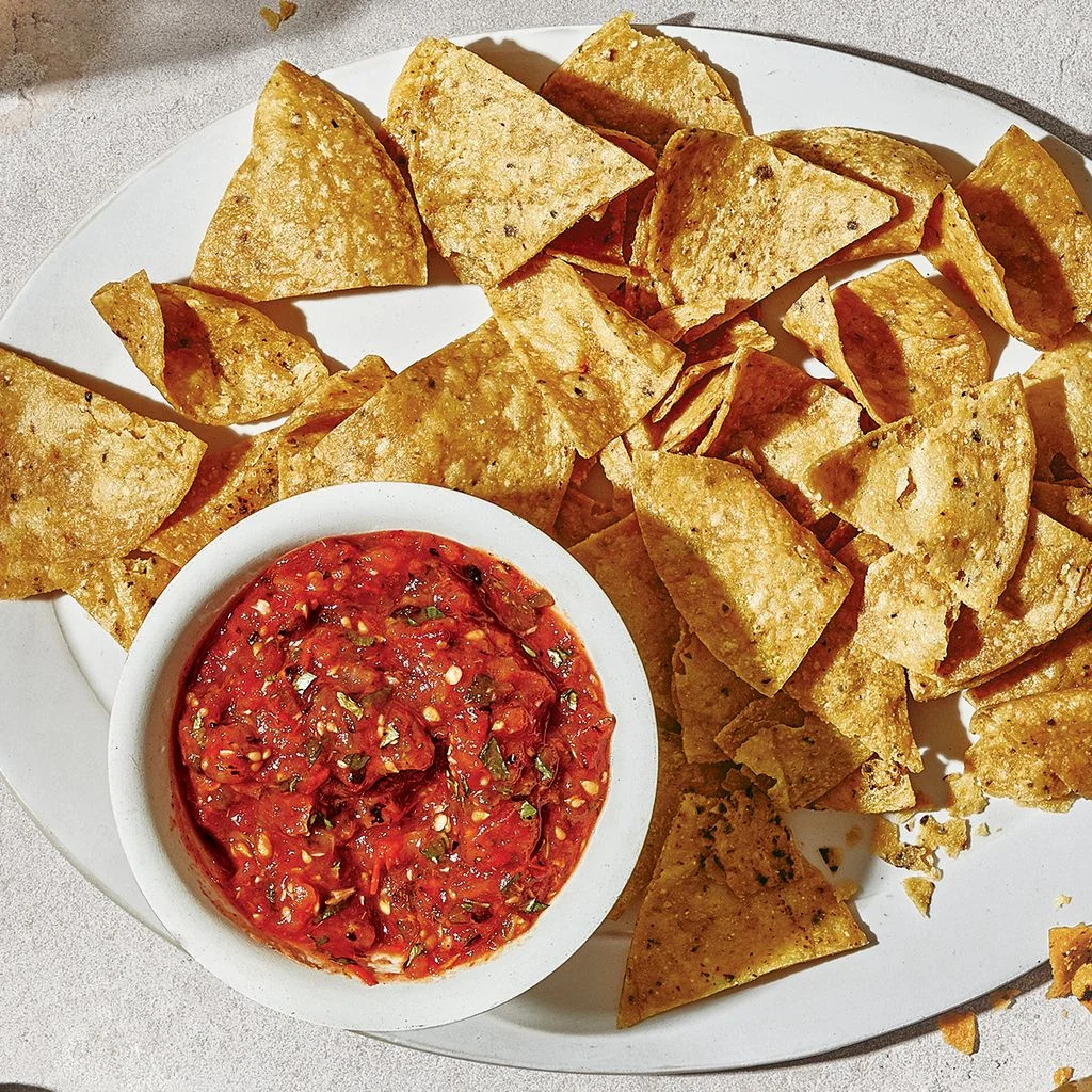 A bowl of fresh tomato salsa on a platter with tortilla chips.