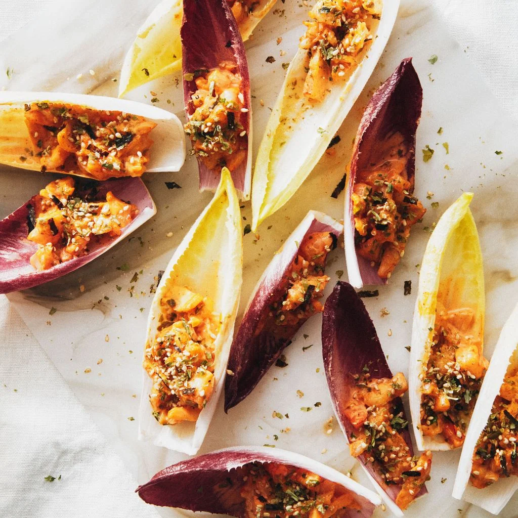 Red and yellow endive spears filled with diced shrimp in a gochujang sauce and topped with furikake.