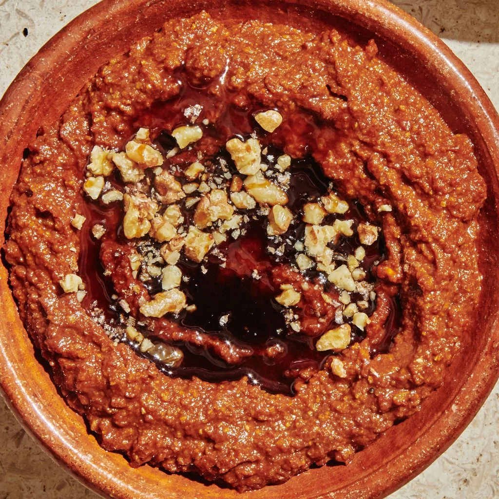 Bowl of muhammara  topped with chopped walnuts and pomegranate molasses.