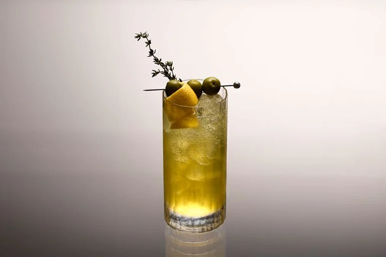 Aperitivo lemon juice olive brine chilled tonic water in a glass with an olive and lemon garnish