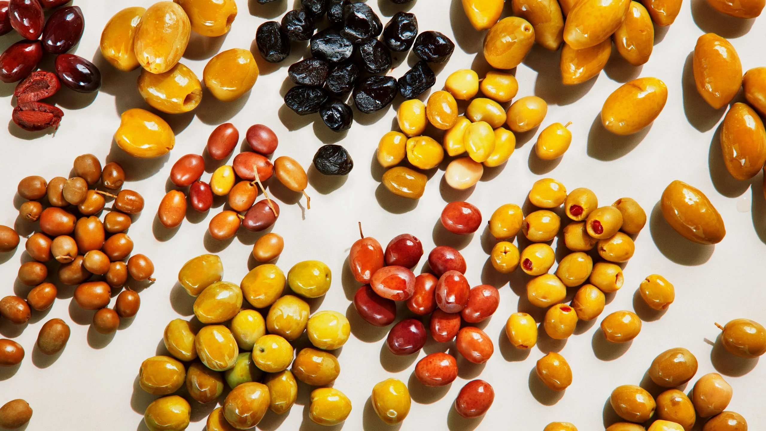 Assorted green purple and black olives including Castelvetrano Kalamata Cerignola Gordal and Niçoise varieties arranged...