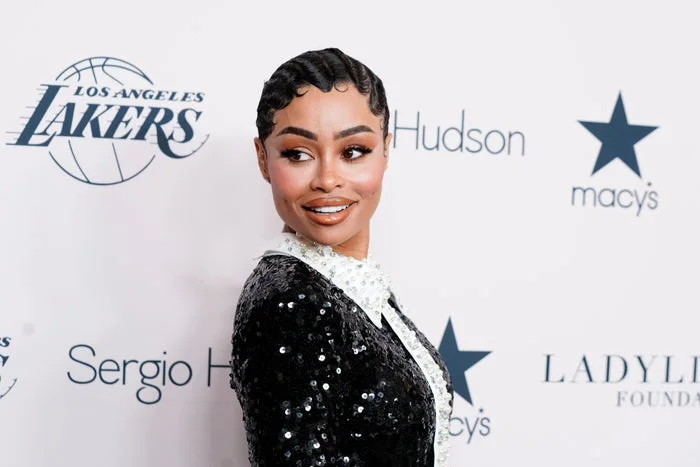 Blac Chyna in a sequined outfit with a collar poses on a red carpet, featuring logos for Los Angeles Lakers and Macy's in the background