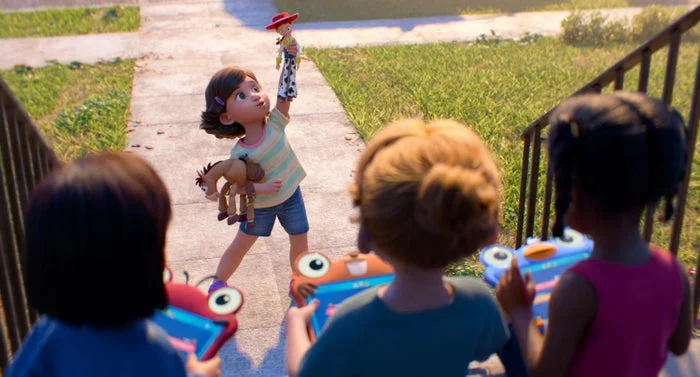 Child holds Woody from Toy Story while three kids with tablets watch. The scene is outside on a sidewalk