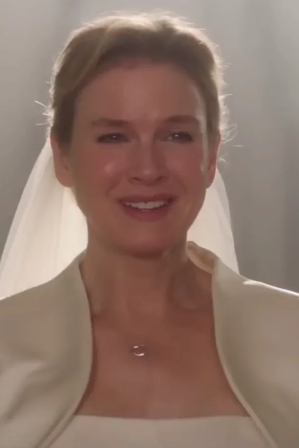Renee Zellweger in elegant bridal attire smiles softly, wearing a simple jacket over a gown and a veil in a scene from Bridget Jones Baby