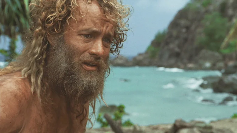 Tom Hanks as Chuck Noland looking dismayed with an overgrown beard and hair in Cast Away