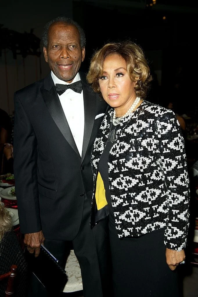 Two individuals at an event; one in a tuxedo and the other in a patterned jacket over a yellow top