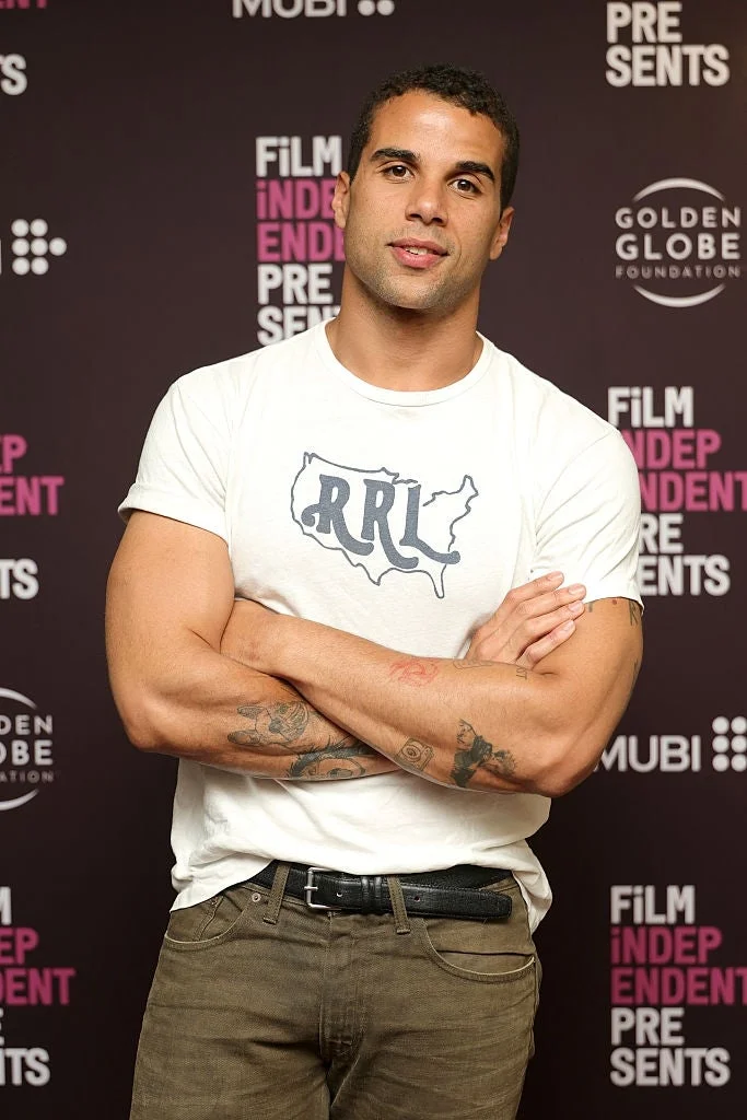 A person standing with arms crossed, wearing a casual t-shirt with a map design. They are attending a Film Independent event