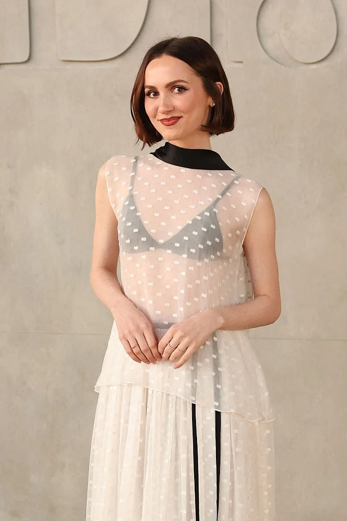 A person in a semi-sheer polka dot dress poses for photos at an event