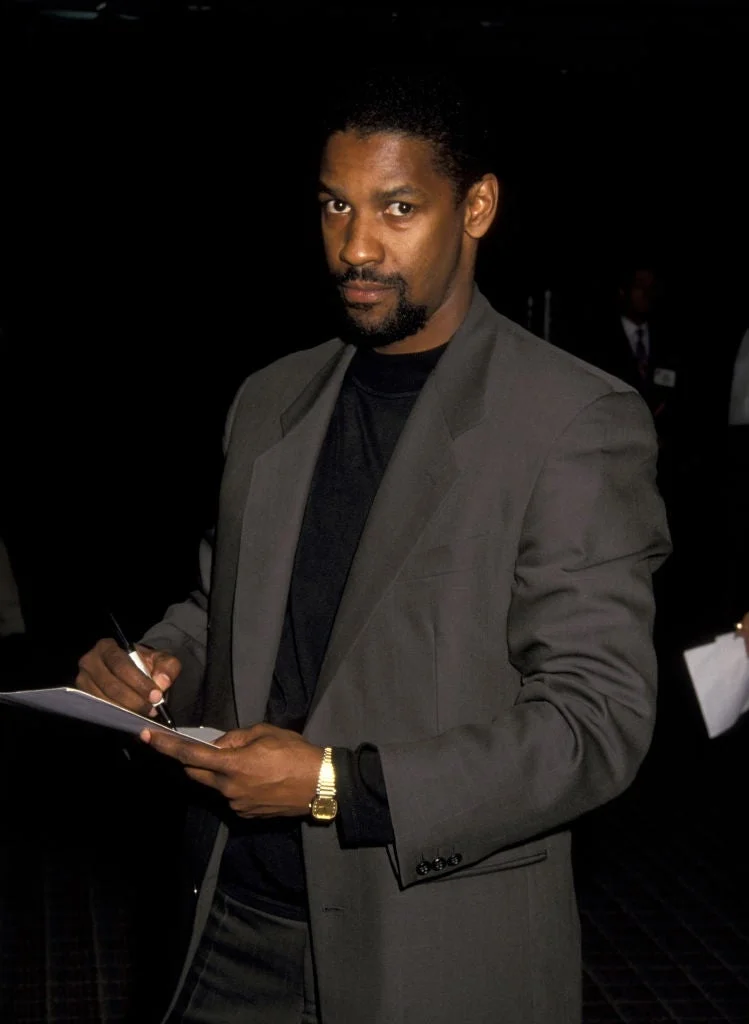 Person in a sharp suit signing autographs at an event, holding a pen and papers