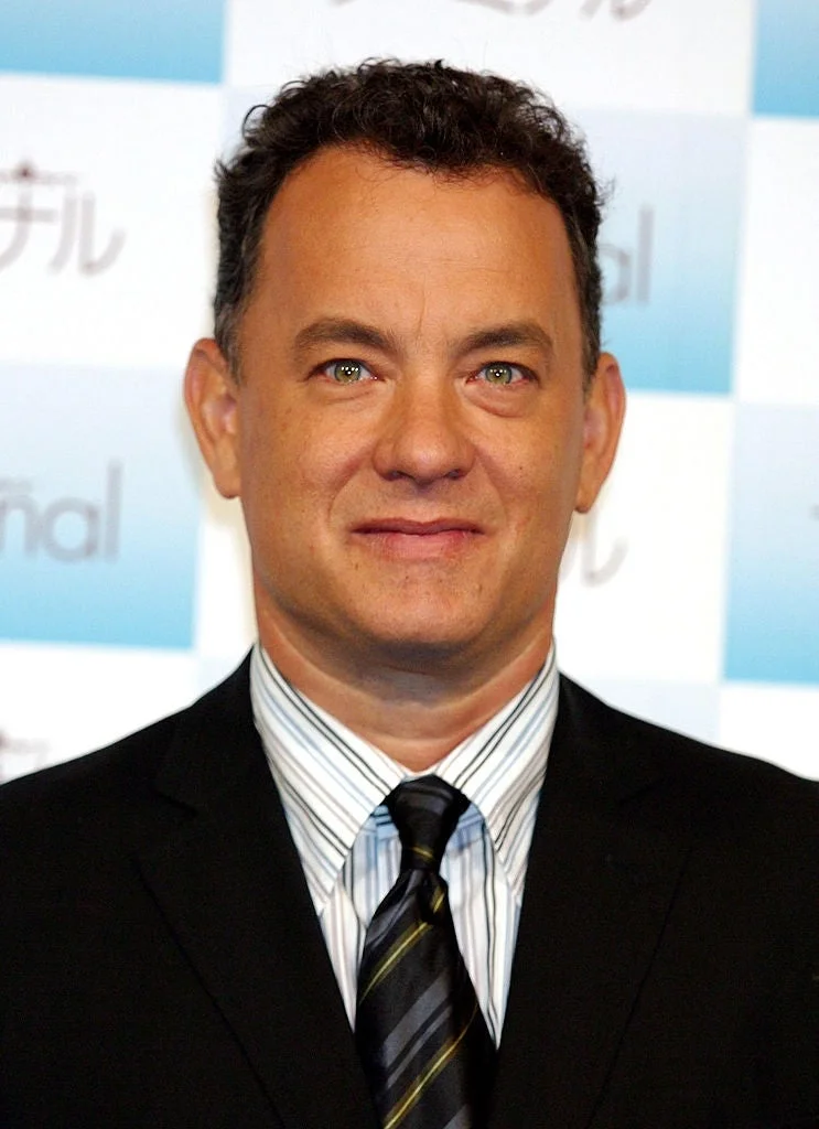 A man in a suit and striped tie stands in front of a checkered backdrop at a media event