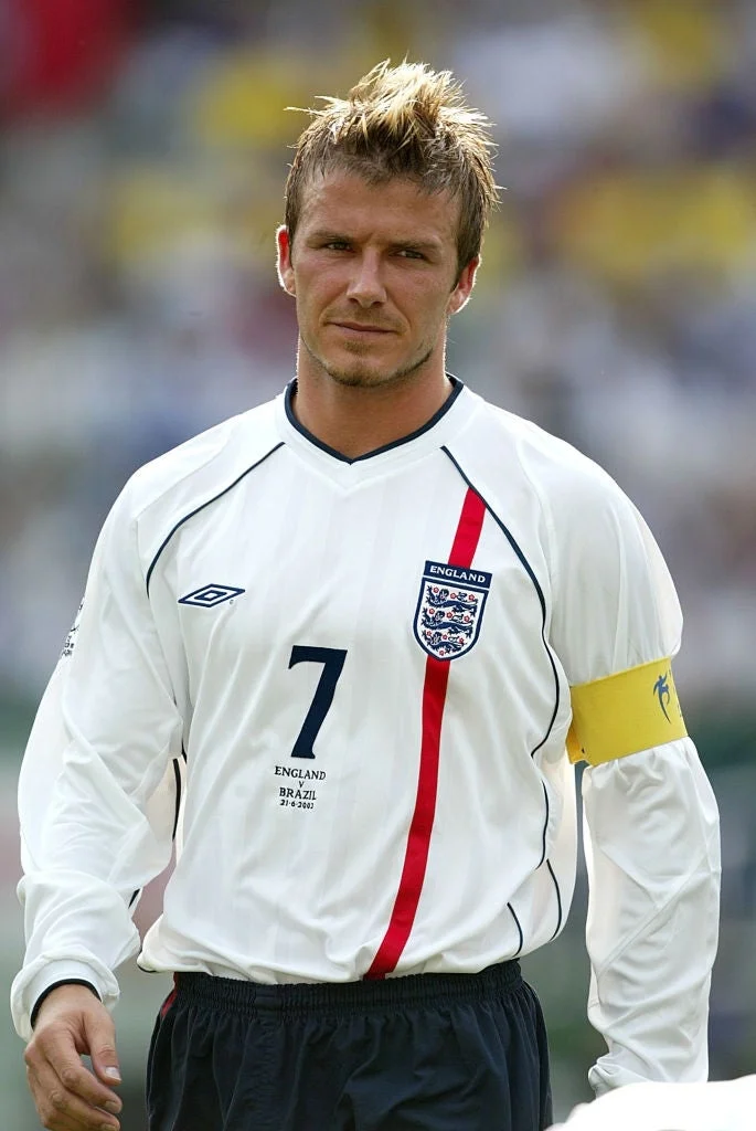 A soccer player wearing an England jersey with a captain's armband, looking focused, is on the field