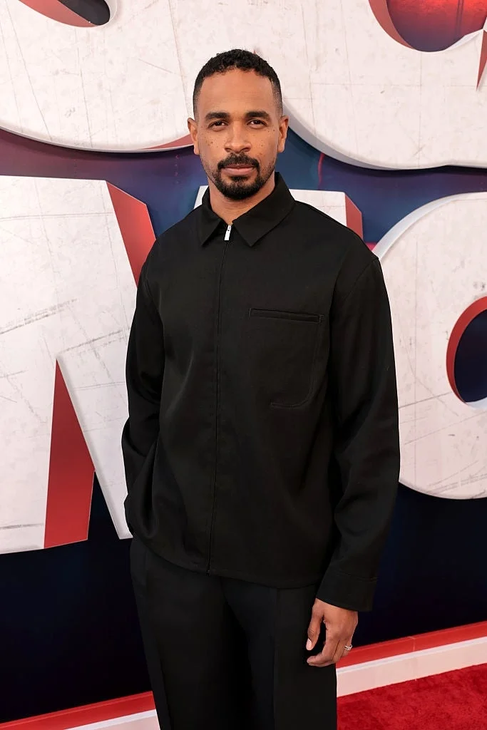 Person on red carpet wearing a minimalist black outfit with a collared jacket